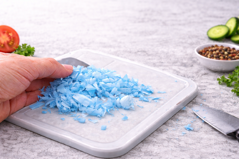 Hand holding a small pile of blue shredded material on a white cutting board with vegetables in the background.
