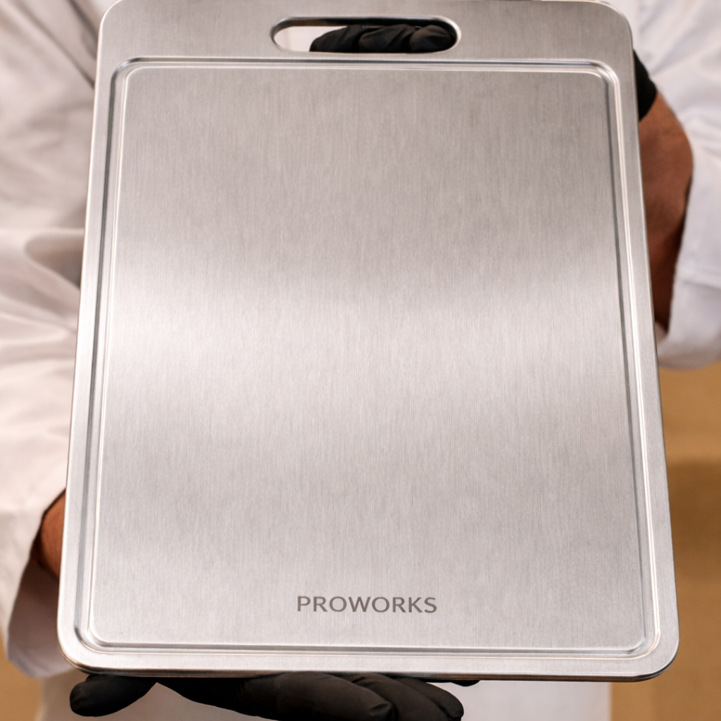 Person holding a metallic baking tray with 'PROWORKS' branding on a wooden surface.
